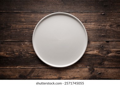 Top view of empty ceramic white plate on wooden background