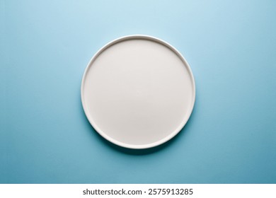 Top view of empty ceramic white plate on blue background