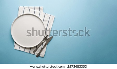 Top view of empty ceramic white plate and cutlery on blue background