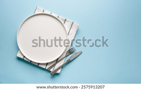 Top view of empty ceramic white plate and cutlery on blue background
