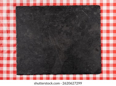 Top view of an empty dark cutting board on checkered red tablecloth, perfect for food presentation or background