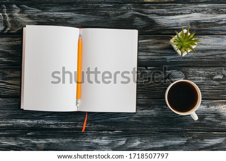 top view of empty notepad, pencil, cup of coffee and succulent on dark wooden surface