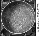 A top view of an empty pan with bubbles and steam rising from it on a black stove