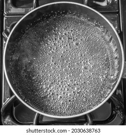 A top view of an empty pan with bubbles and steam rising from it on a black stove