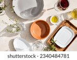 Top view of empty plates, clear glasses with prominent shadows on a textured white table with bright sunlight. Perfect for food or product design and advertising.