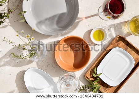 Top view of empty plates, clear glasses with prominent shadows on a textured white table with bright sunlight. Perfect for food or product design and advertising.