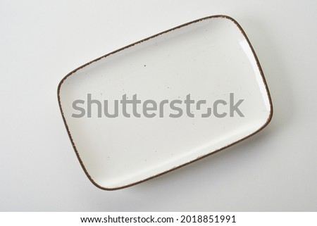 Top view of empty rectangular shaped white ceramic serving platter with dark rim on white background