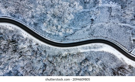 Top view of empty road along winter forest after snowfall. Aerial view of winding road through trees covered with snow - Powered by Shutterstock