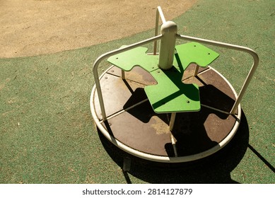 Top view of empty round merry go round with green seats on rubber playground surface. Metal spinning carousel equipment, outdoor children entertainment on sunny summer day