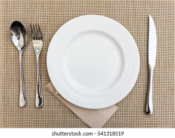 Top View. Empty White Plate For Food With Fork And Spoon Set On Brown Weave  Background  