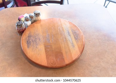 Top View An Empty Wooden Table With Rotating Serving Plate And Shaker Seasonings. Red Pepper Flakes, Parmesan, Black Pepper, Salt