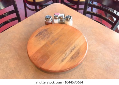 Top View An Empty Wooden Table With Rotating Serving Plate And Shaker Seasonings. Red Pepper Flakes, Parmesan, Black Pepper, Salt