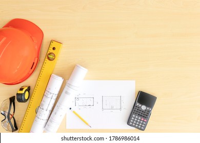 Top view engineer desk light brown wood texture have roll home plan and tools, measuring tape , calculator, hardhat with copy space.House plan on wood table architect have safety glasses and workplace