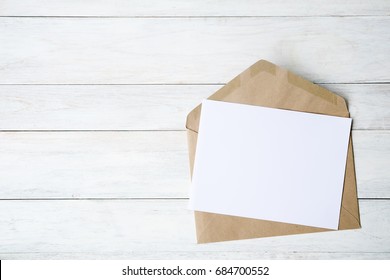 Top view of envelope and blank greeting card with rose flowers on white wooden background.