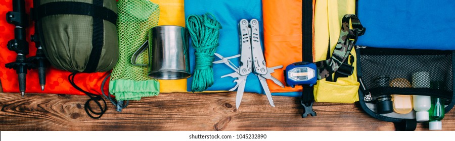 Top view of equipment for hiking and travel on wooden background . Items include trekking pole, multi tool, flashlight, hygiene products, tracking clothes - Powered by Shutterstock