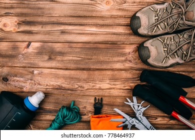 Top View Of Equipment For Hiking And Travel On Wooden Table With Empty Space In The Middle. Items Include Trekking Pole, Shoes, Multi Tool, Hermetic Bag, Rope, Water Bottle