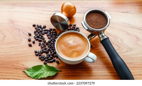 Top view of Espresso coffee cup and equipment of barista coffee tool portafilter with tamper and dark roasted coffee beans with green coffee leaf  on wooden table