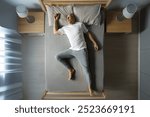 Top view of European middle aged man in pajamas sleeping on his back in comfortable bed without blanket, full length horizontal shot