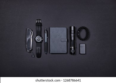 Top view of everyday carry (EDC) items for men in black color - folding knife, lighter, note book, tactical pen, watch, paracord survival bracelet and flashight. Flat lay. Minimal concept. 