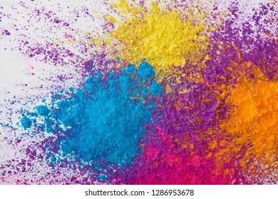 top view of explotion of yellow, purple, orange and blue holi powder on white background