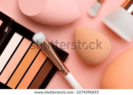 Top view of eyeshadow, makeup sponges and makeup brushes over pink background. Beauty and makeup concept