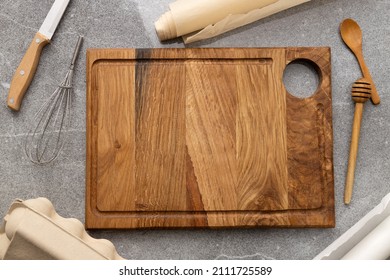 Top View F Wooden Empty Cutting Board,knife,whisk,baking Paper,eggs Paper Box,wooden Spoon,honey Dipper On The Grey Table