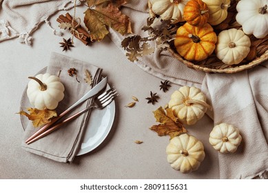 Top view of fall table setting with white mini pumpkin, fork, knife, cinnamon, spices and dry leaves..
