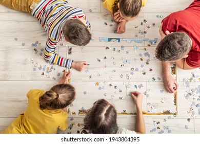 Top view of a family assembling puzzle on the floor at home.
