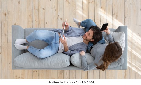 Top View Of Family Husband And Wife Sitting On Couch, Using Tablet And Smartphone, Panorama