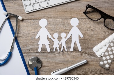 Top view of family paper chain on a doctor desk. Medical worktable with keyboard, blue stethoscope, pills and eyeglasses. Family healthcare, medicine and insurance concept.