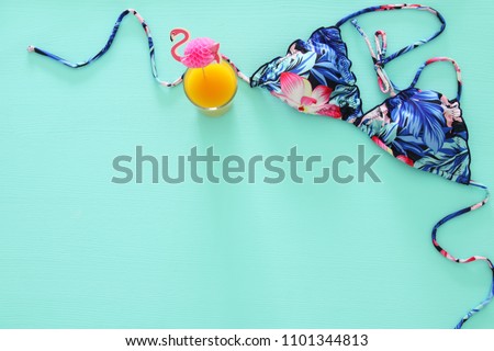 Top view of fashion female swimsuit bikini, fruit coctail on mint wooden background. Summer beach vacation concept