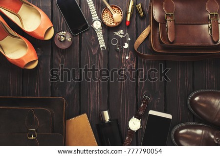 Top view, fashionable male and female personal items with space on a dark wooden background. Leather bag, shoes, watches, stylish accessories.