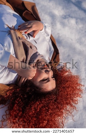 Top view of a fat red-haired woman lying on the snow.