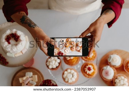 Top view of female baker using smart phone while photographing sweet food laying on the table