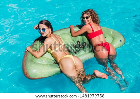 Top view of female friends wearing bikini lying on an inflatable toy in pool. Woman sunbathing on floating pool inflatable toy.