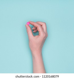 Top View Of Female Hand Holding Pink Prescription Pill Over Pastel Blue Background. Sick Patient Taking Medication.