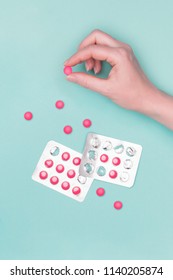 Top View Of Female Hand Holding Pink Prescription Pill Next To Blister Packs Over Pastel Blue Background. Sick Patient Taking Medication.