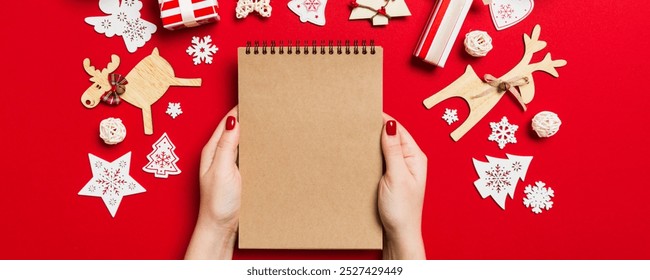 Top view of female hand making some notes in noteebok on colorful background. New Year decorations and toys. Christmas time concept. - Powered by Shutterstock