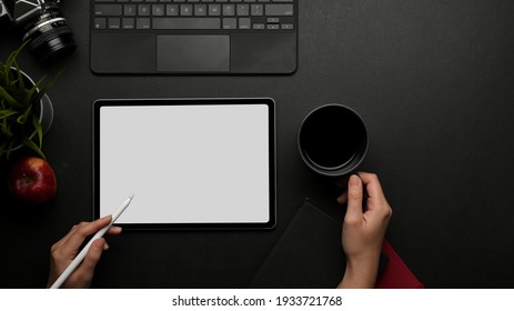 Top view of female hand working with digital tablet and holding coffee cup on dark creative workspace, clipping path - Powered by Shutterstock
