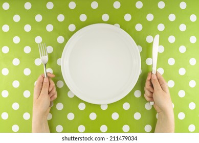 Top View Of Female Hands At Dinner Table Holding Fork And A Knife Above Empty Flat White Plate, Dieting Concept.