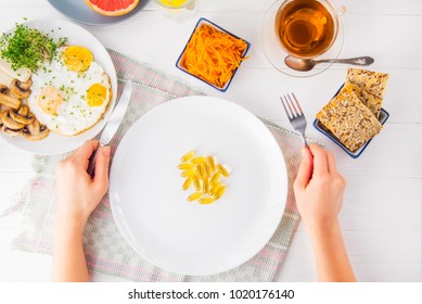 Top View Female Hands Holding Knife And Fork And White Plate With Vitamin Pills On The Served Wooden Table With Breakfast Meal. Pill Instead Of Food. Healthy Diet Concept. Selective Focus