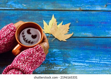 Top View Female Hands Holding Tea Cup With Scary Ghost Face On Wooden Blue Boards Background. 