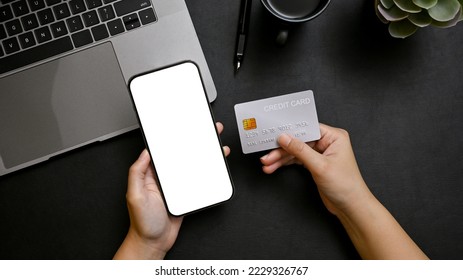 Top view, A female hands holding a smartphone white screen mockup for display your graphic ads and credit card over modern black office desk. online payment, mobile banking, online shopping - Powered by Shutterstock