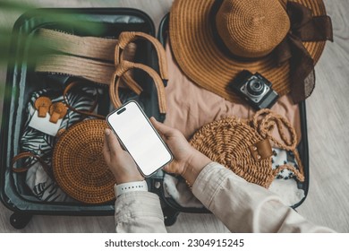 Top view of female hands holding smartphone with blank screen near suitcase with beach accessories on wooden floor. - Powered by Shutterstock