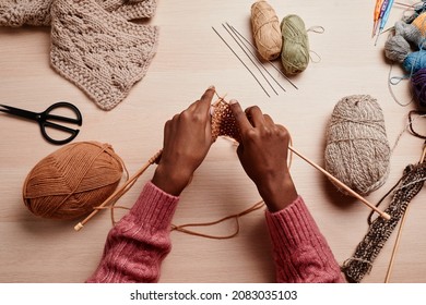 Top view of female hands knitting against wooden table in cozy light, copy space