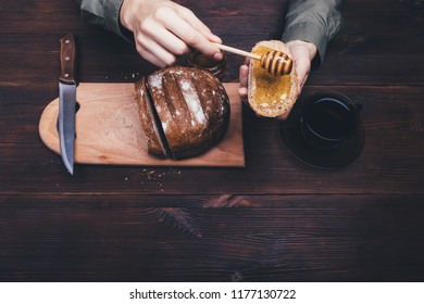 Top view female hands make sandwich of rye bread and honey on dark wooden table next to cup of black tea or coffee. Composition of simple rustic food. - Powered by Shutterstock