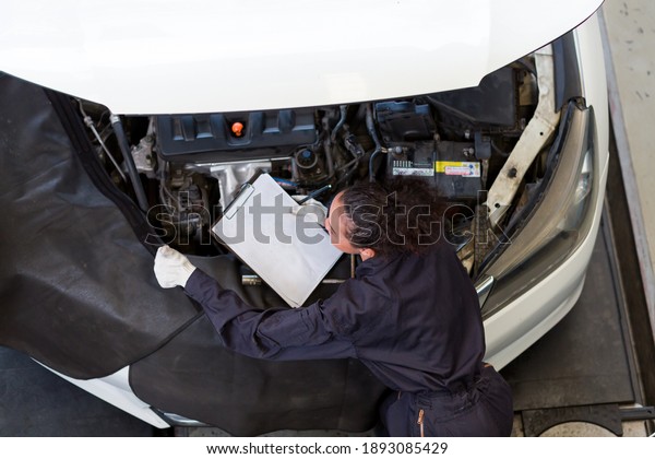 Top view of female mechanic working at the\
garage. Professional female car mechanic examining, repair and\
maintenance under hood of car at auto car repair service. Car\
service and Maintenance\
concept
