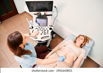 Top View Of Female Patient Lying On Daybed While Having Ultrasonography Procedure In Clinic. Woman Sonographer Doing Abdominal Ultrasound Scanning For Patient. Concept Of Healthcare And Sonography.