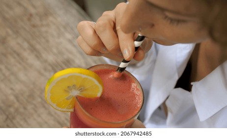 Top view of female swirling her berry smoothie with sustainable paper straw and takes drinks it. Wooden table on the background