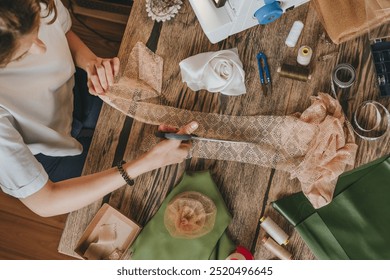 Top view of female tailor cutting lace with scissors making handmade decor flower. Working place for tailoring at home or workshop. Upcycling clothes concept. - Powered by Shutterstock